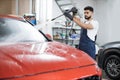 Handsome man worker washing modern red car hood under high pressure water in car wash service Royalty Free Stock Photo