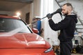 Handsome young man worker washing modern red car under high pressure water in car wash service. Royalty Free Stock Photo