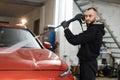 Handsome young man worker washing modern red car under high pressure water in car wash service. Royalty Free Stock Photo