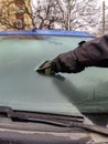 Cleaning car windows in winter. Man scrapes hoarfrost with a plastic scraper from the windshield of a blue car. Royalty Free Stock Photo