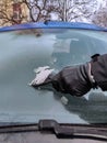 Cleaning car windows in winter. Man scrapes hoarfrost with a plastic scraper from the windshield of a blue car. Royalty Free Stock Photo