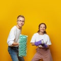 Cleaning concept. Happy young couple man and woman with household tools in hands posing against yellow studio wall banner Royalty Free Stock Photo