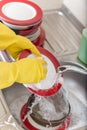 Cleaning dishware kitchen sink sponge washing dish. Close up of female hands in yellow protective rubber gloves washing Royalty Free Stock Photo