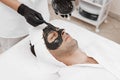 Spa therapy for men receiving facial black mask. Royalty Free Stock Photo