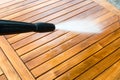 Cleaning garden acacia table with a power washer - high water pressure cleaner on wooden exotic table surface - focus on the tip