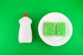 Cleaning green sponges on a white plate and detergent for dishes on a green background. Top view, flatlay, close up. Concept Royalty Free Stock Photo