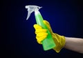 Cleaning the house and cleaner theme: man's hand in a yellow glove holding a green spray bottle for cleaning on a dark blue Royalty Free Stock Photo