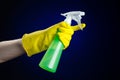 Cleaning the house and cleaner theme: man's hand in a yellow glove holding a green spray bottle for cleaning on a dark blue Royalty Free Stock Photo