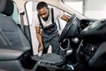 Cleaning of interior of the car with brush, car detailing service. Young pleasant black man doing car interior and seat