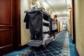 Cleaning at its finest. Full-length shot of hotel maid in uniform walking along the hall with chambermaid trolley. Room