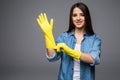 Cleaning lady getting spring cleaning ready putting on rubber gloves. Cleaning woman smiling happy at camera isolated on grey back