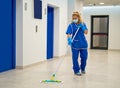 A cleaning lady with a mask on her face cleans the hallway Royalty Free Stock Photo