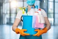 A cleaning lady in a mask holds a bucket of cleaning products