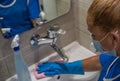 A cleaning leady with mask on her face cleans the washbasin