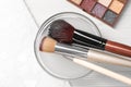 Cleaning makeup brushes in bowl with special liquid on white wooden table, flat lay Royalty Free Stock Photo