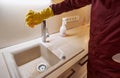 Cleaning person in uniform sponging kitchen faucet