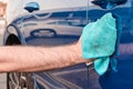 Cleaning or polishing of a blue car with microfiber cloth. Manual car washing service.