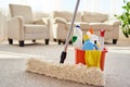 Cleaning set for different surfaces in orange bucket and mop on floor in living room, copy space. Cleaning service concept. Royalty Free Stock Photo