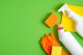 Cleaning supplies on green background. Top view cleaner spray bottle, rag, sponge, detergent, rubber gloves. House cleaning