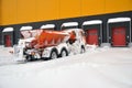Cleaning the territory of a modern warehouse complex from snow accumulations with specialized road equipment.