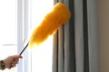 Cleaning the window and curtains area with a fluffy yellow duster Royalty Free Stock Photo