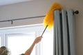 Cleaning the window and curtains area with a fluffy yellow duster