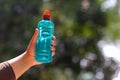 Clear blue green water bottle, the lid is red with a hole in the center for portability, natural background. With the hand held Royalty Free Stock Photo