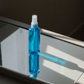 A clear blue spray bottle with a white nozzle sits on a reflective glass surface, casting Royalty Free Stock Photo
