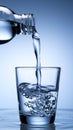 Bottle pouring water into glass, dynamic stream against blue background