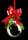 Clear Christmas ornament hanging by red ribbon rope with the bauble surrounded with green mistletoe