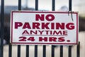 Red and White No Parking Anytime 24 Hrs Sign Mounted on a Metal Fence