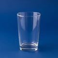 Clear cylindrical glass standing upright on a solid blue background Royalty Free Stock Photo