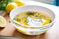 clear detox broth with floating herbs and lemon slices, detoxifying