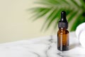 Clear dropper bottle with towel on marble table, green palm leaf on the background. Amber glass essential oil container, SPA