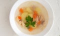 Clear fish soup with pieces of vegetables and percussion in a white bowl on a white plate.