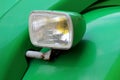 Clear front headlight of old light green vintage car mounted on rusted metal pipe Royalty Free Stock Photo