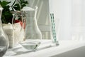 A clear glass carafe of water and a glass with striped tubes on a table with a white tablecloth in the morning sun.