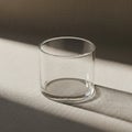 A clear glass cylinder is placed on a textured beige surface. The glass is empty and Royalty Free Stock Photo
