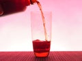 In a clear glass filled with a dark fizzy drink. Photo on a pink background