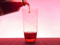 In a clear glass filled with a dark fizzy drink. Photo on a pink background