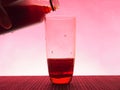 In a clear glass filled with a dark fizzy drink. Photo on a pink background
