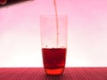 In a clear glass filled with a dark fizzy drink. Photo on a pink background