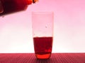 In a clear glass filled with a dark fizzy drink. Photo on a pink background