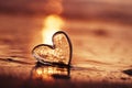 Clear glass heart on sand beach with sunrise sun light