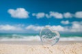 Clear glass heart on white sand beach,