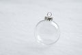 A clear glass holiday ornament rests on a soft white snow surface in a bright winter scene. Royalty Free Stock Photo