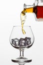 Clear glass glass with ice cubes. Frozen stream from a bottle of whiskey or cognac or brandy on a white isolated background Royalty Free Stock Photo