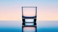 A clear glass sits on a reflective surface, with a gradient background of blue and pink. Royalty Free Stock Photo