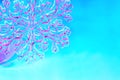 Clear glass snowflake in pink neon light on blue background