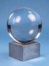 Clear Glass Sphere Resting on a Metallic Cube Against a Serene Blue Backdrop in an Artistic Display Setting Royalty Free Stock Photo